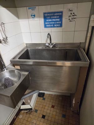 deux lavabos dans des toilettes publiques, avec une affiche accrochée au mur