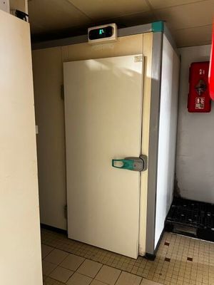 un réfrigérateur blanc dans une pièce où se trouve une borne d'incendie rouge accrochée au mur