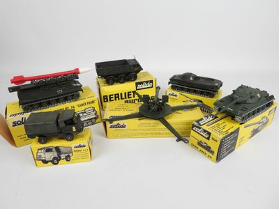 trois jouets représentant des véhicules militaires, emballés dans leur boîte, posés sur une surface blanche