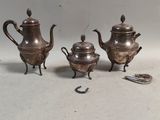 trois théières en argent et une cuillère posées sur une table