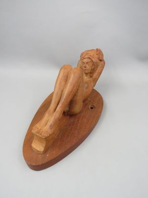 sculpture en bois représentant un homme assis sur une planche de surf, posée sur une surface blanche