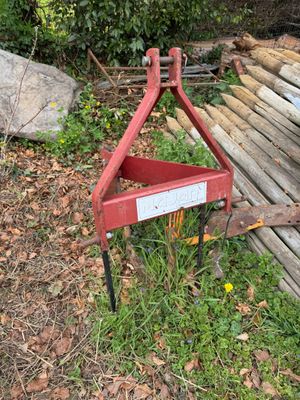 a red plow sitting in the grass next to a pile of wood