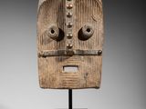 une image représentant un masque en bois posé sur un socle, sur une surface blanche