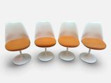 quatre chaises « Tulip » avec des coussins orange et des piètements blancs