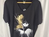 Le t-shirt est noir et doré, avec une fleur blanche dessus.