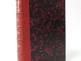 an old red and black book sitting on top of a white surface