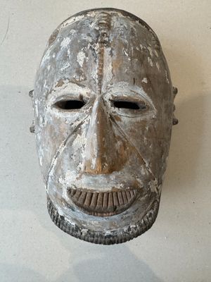 a wooden mask hanging on a wall with a white background