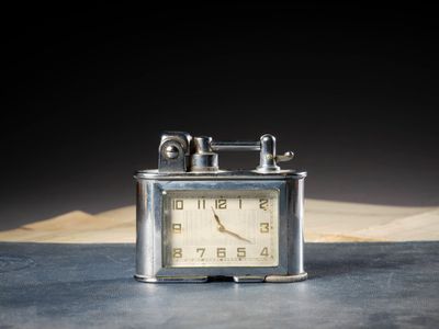 une petite horloge en argent posée sur une table, avec un livre en arrière-plan