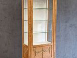 une vitrine en bois avec des étagères en verre, posée sur un parquet
