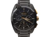 La montre est noire et dorée, avec un cadran noir et des aiguilles dorées.
