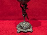 une coupe antique en bronze posée sur un socle, sur fond rouge