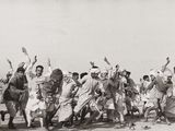 photographie en noir et blanc d'un groupe d'hommes dansant dans le désert