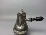 une théière ancienne en argent avec une poignée noire sur une surface blanche