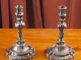 une paire de bougeoirs en argent posés sur une table en bois, avec des rideaux rouges en arrière-plan