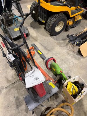 Plusieurs tondeuses à gazon sont alignées dans un garage, avec des outils posés par terre.