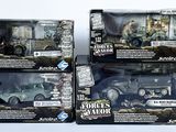 trois jouets représentant des véhicules militaires, présentés dans leurs boîtes, posés sur une surface blanche
