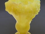 yellow glass vase with a flower inside of it on a gray surface