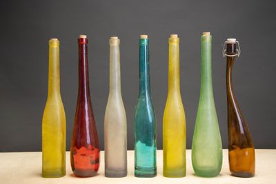Plusieurs bouteilles en verre de différentes couleurs sont alignées sur une table