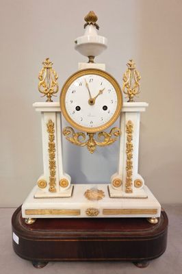 une horloge blanche et dorée posée sur un socle en bois