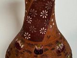 a brown vase with flowers on it sitting on a white surface