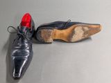 pair of black leather shoes with red soles on a grey surface