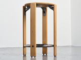 a wooden stool with a black seat in a white room