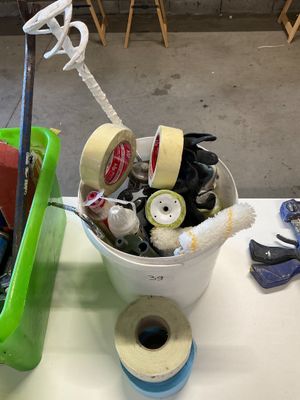 a bucket full of tape, scissors and other items on a table