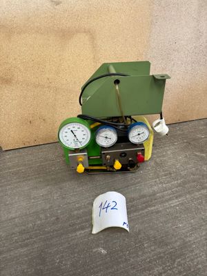 a small green machine with two gauges next to a roll of toilet paper