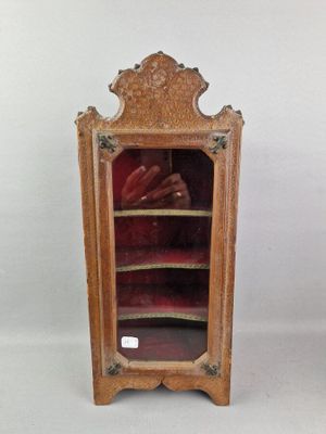 une vieille vitrine en bois contenant des chaussures, posée sur une surface blanche