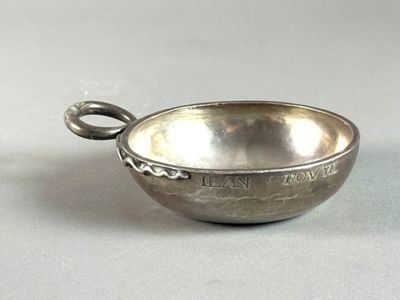 an old silver bowl with a handle on a white surface