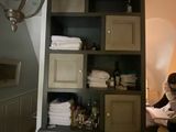 une femme debout dans une salle de bains, avec une serviette posée sur une étagère