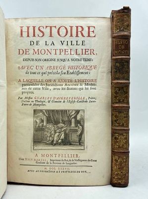 un vieux livre ouvert posé sur une table, à côté d'une pile de livres