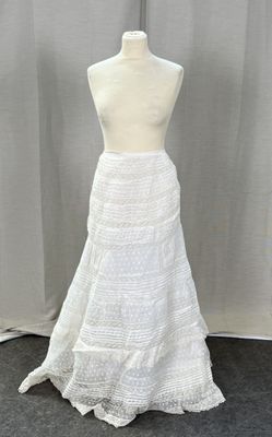 a white dress on a mannequin stand with a white curtain behind it