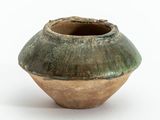 un vase vert et marron posé sur une surface blanche