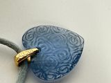 a blue glass pendant with a gold clasp on a gray cord