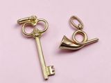 pair of gold plated key charms on a pink background