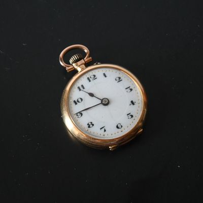 a gold pocket watch with a white face on a black surface