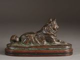 statue of a dog laying down on a wooden base on a gray background