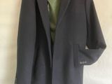 un manteau gris suspendu à un cintre sur un drap blanc, avec une chemise verte en dessous
