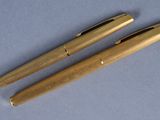 two golden colored pens sitting next to each other on a blue surface