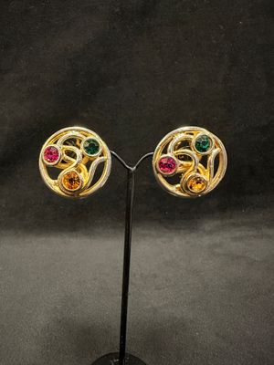 a pair of gold earrings with multi colored stones on a stand