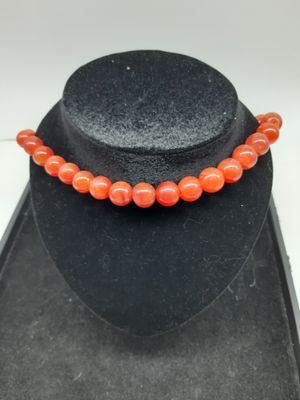 un gros plan d'un collier porté par un mannequin, orné d'une perle orange