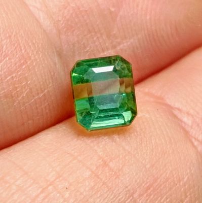 a close up of a person ' s hand holding a green emerald stone
