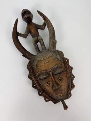 une image représentant un masque en bois sur lequel est assis un homme