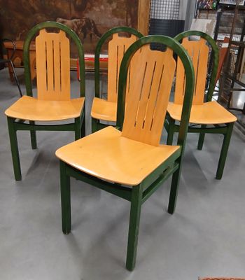 Quatre chaises en bois sont alignées dans une pièce, avec un tableau accroché au mur derrière elles.