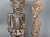 deux statues en bois représentant des personnes debout l'une à côté de l'autre sur une surface grise