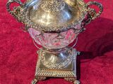 an ornate silver plated bowl on a stand on a red carpet