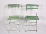 pair of green metal folding chairs against a white background