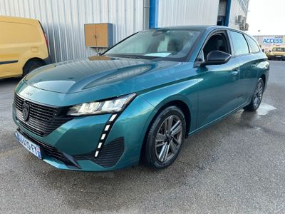 une voiture bleue garée devant un immeuble, avec une camionnette en arrière-plan