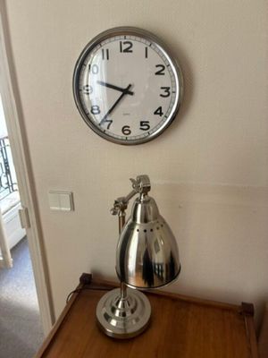 une horloge accrochée au mur, à côté d'une lampe posée sur une table